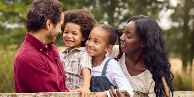 Loving Mixed Race Family Leaning On Fence On Walk In Countryside